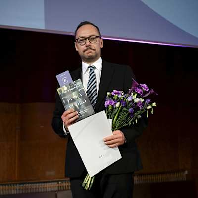 Pavo Teittinen pitelee kädessään kirjaa ja kukkia.