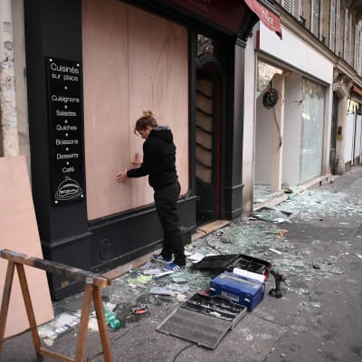 En kvinna i Paris ersätter ett krossat skyltfönster med plywoodskivor på söndag morgon. 