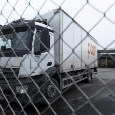 Lastbil med Postens logga står parkerad bakom ett stängsel.