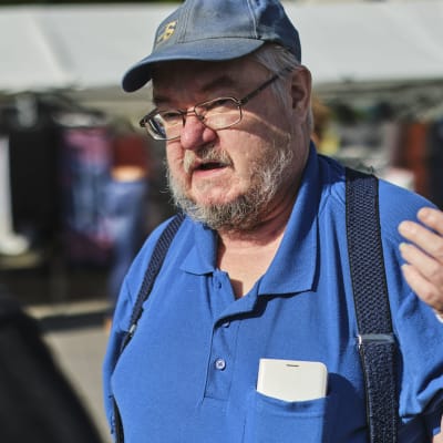 Sannfinländaren Pekka Kataja står på ett torg och pratar. Han håller ena armen uppe, den är täckt i gips. 
