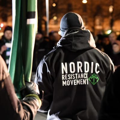 Nordiska motståndsrörelsens marsch i Helsingfors på självständighetsdagen 2017. En man har på sig en jacka med organisationens namn tryckt på ryggen.