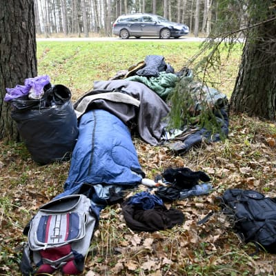 Makuupusseja ja tavaroita metsässä tien vierustalla.
