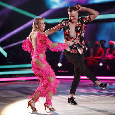 Kvinna i rosa dansdräkt ler och dansar på en scen med en man.