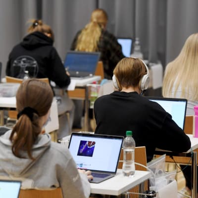 Gymnasieelever under ett provtillfälle med ryggarna vända mot kameran.