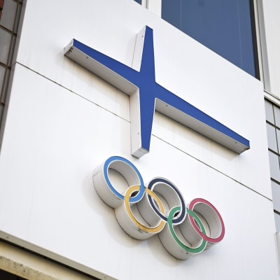 Olympiarenkaat ja Suomen lippua kuvastava sininen risti talon seinässä.