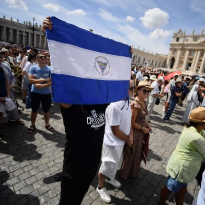 En man håller upp Nicaraguas flagga på Petersplatsen i Rom. Alla människor är vända mot Apostolska palatset, men påven syns inte på bilden.