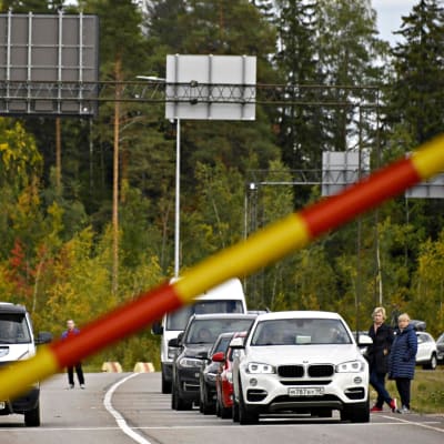 Bilar i kö vid rysk-finska gränsen i Vaalimaa. Två kvinnor står utanför en bil, i förgrunden en bom.