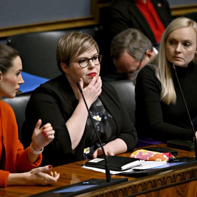 Sanna Marin, Annika Saarikko och Maria Ohisalo sitter vid ett bord i riksdagen.