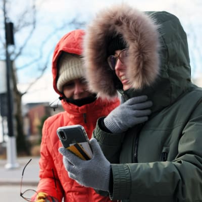 Två personer som har på sig tjocka vinterjackor med huvor neddragna över pannan. De har röda nästippar och det ser ut att vara kallt.