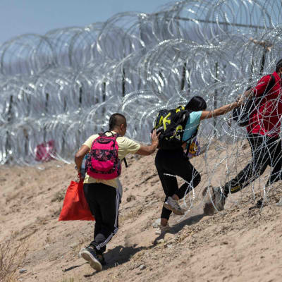 Invandrare går igenom raktråd som omger ett provisoriskt migrantläger i El Paso.