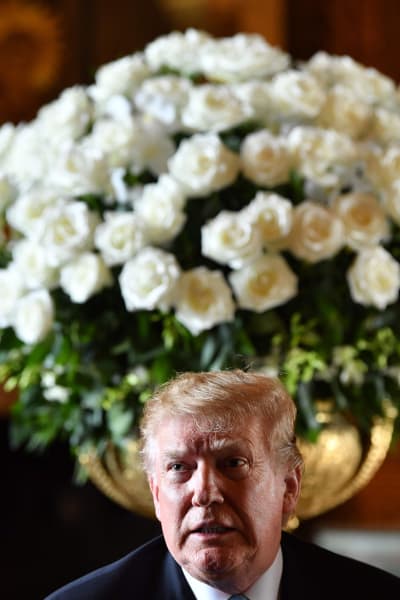 Donald Trump i Mar a Lago framför en jättebukett vita blommor i vas.