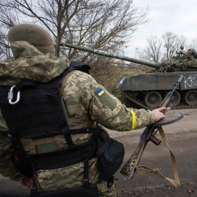 Ukrainalainen sotilas pitää kädessään konekivääriä. Taustalla tuhoutunut panssarivaunu.