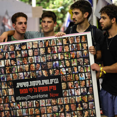 En grupp män håller upp en affisch med bilder av gisslan och texten Bring them home, ta hem dem.