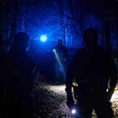 Poliisit valaisevat taskulampuilla pimeää metsää.