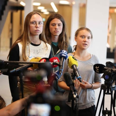 Greta Thunberg talar till pressen i Malmö tingsrätt. Bredvid henne står två andra unga människor.