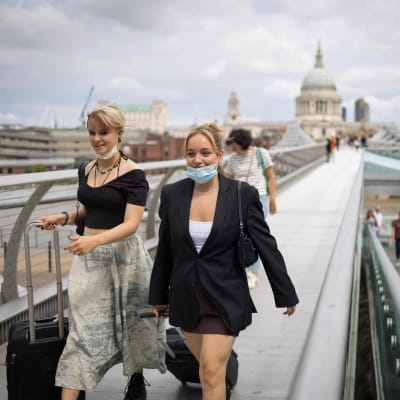 Två unga kvinnor går på Millennium Bridge i London. De bär munskydd under sina hakor.