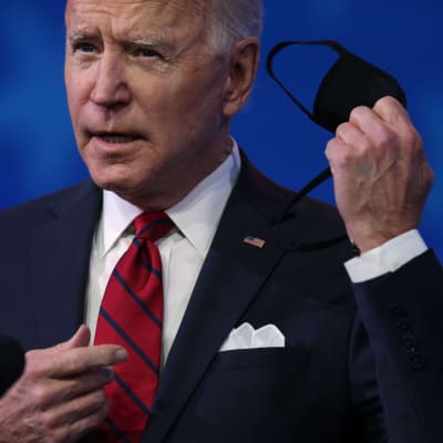 Närbild av Joe Biden som tar av sig ett svart munskydd.