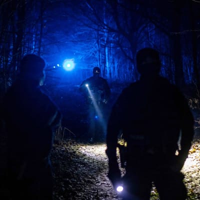 Poliisit valaisevat taskulampuilla pimeää metsää.
