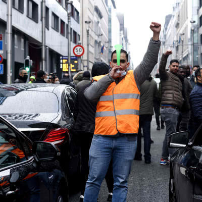 En man i reflexväst står och demonstrerar för Uberchaufförers rättigheter i Bryssel. Bakom honom syns fler demonstranter och runtom honom svarta bilar.