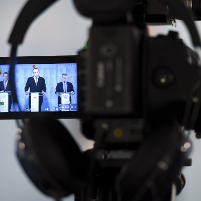 En kamera filmar försvarsminister Jussi Niinistö som håller presskonferens.