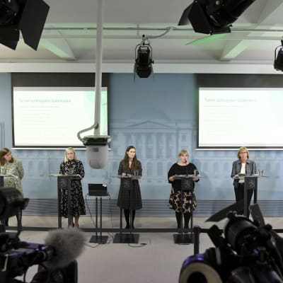 Partiledarna för partierna i Sanna Marins regering, plus finansminister Matti Vanhanen, står på rad under regeringens presskonferens.