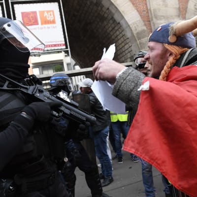 En man inklädd i den franska seriekaraktären Obelix höjer händerna mot en beväpnad och maskerad polis.