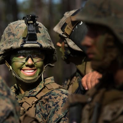 En soldat i utrustning och grönmålad i ansiktet ler.