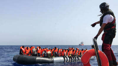 En av räddningspersonalen från fartyget Ocean Viking står på kanten av en gummibåt och förbereder sig för att rädda migranter som sitter på en annan gummibåt ute på havet.