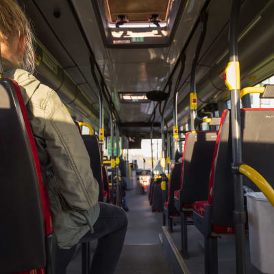 En passagerare sitter inne i en buss. Det finns inte några andra passagerare.