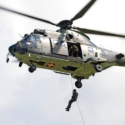 En grön helikopter med soldater i i luften.