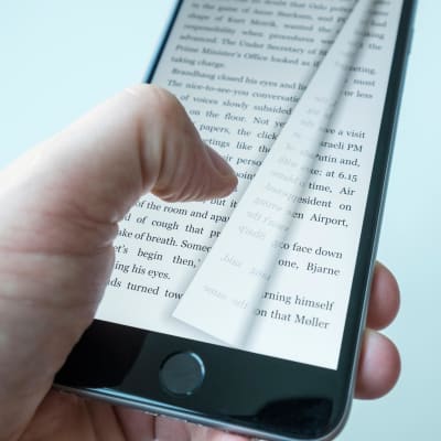 En tumme trycker på en mobiltelefon som har en text på sig och just nu byts sidan.