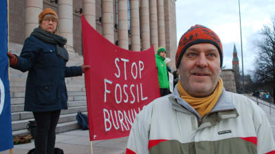 Klimatdemonstrant på riksdagens trappa, med röd banderoll med texten "Stop fossil burning".