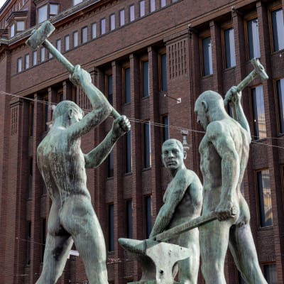 Statyn Tre smeder och i bakgrunden Stockmanns varuhus i Helsingfors centrum.