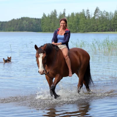 Melina Holmberg ratsastaa hevosella rantavedessä.