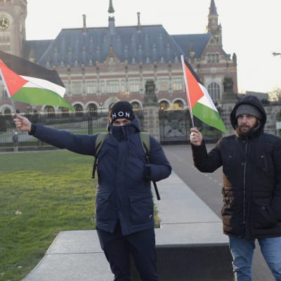 Två palestinska demonstranter med flaggor framför Internationella domstolens byggnad i Haag