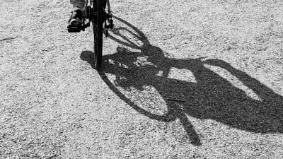 En fot som trampar en cykel över grus och cykelns skugga är enorm på grusplanen.