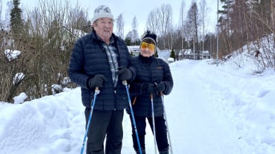 En äldre man och en kvinna poserar med stavar på en snöig väg.