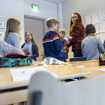 Kuvaamataidon opettaja jakaa ohjeita neljäsluokkalaisten oppilaiden ympäröimänä