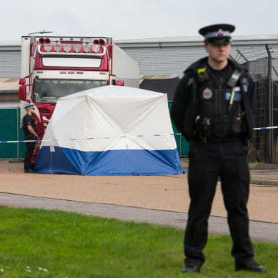 Till höger en polis. I bakgrunden ett blåvitt tält och bakom det en röd lastbil.
