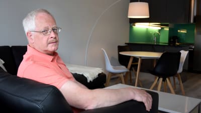 Berndt Huldin sitter i en svart lädersoffa. I bakgrunden skymtar ett köksbord och ett kök.