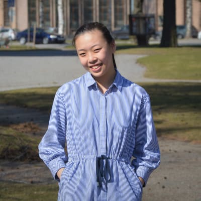 En leende kvinna står i en park.