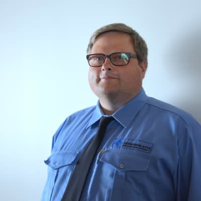 ledande nödcentralsoperatör ralf björklund i blå skjorta med vit vägg i bakgrunden.