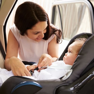Kvinna spänner fast barn i bilbarnstol.