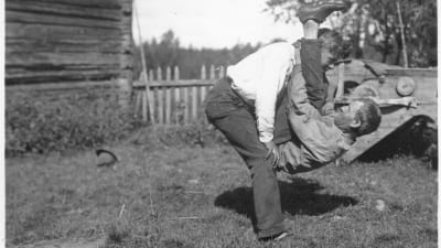 Två män leker leken "prova nacken", där den ena ska lyfta upp den andra med bara styrkan av sin nacke. Bilden är tagen 1932 i Terjärv.