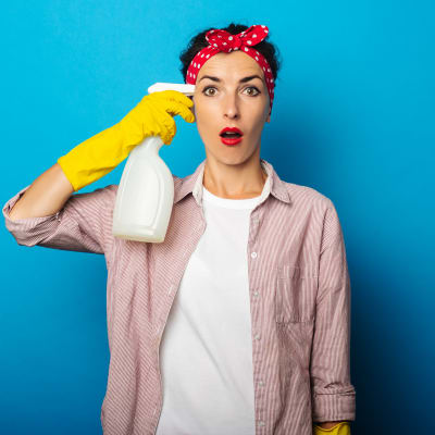 Kvinna med städutrustning riktar tvättmedelsflaska mot tinningen 