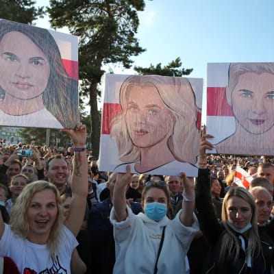 Kvinnor håller upp plakat med bilder på centrala oppositionsfigurer under en demonstration i Minsk.