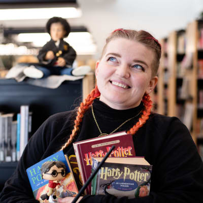 Nainen seisoo kirjastossa kädet täynnä Harry Potter -kirjoja.