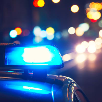 En polisbils blåljus lyser i natten med gatulyktor och billjus i bakgrunden.