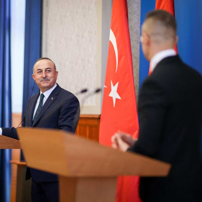 Mevlüt Çavuşoğlu står vid ett talarpodium och tittar på Péter Szijjártó som står vid ett annat talarpodium.