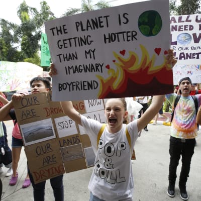 En klimatdemonstrant håller upp ett plakat med texten "The climate is getting hotter than my imaginary boyfriend".